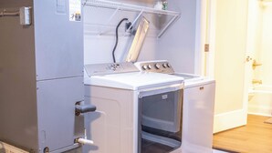 A compact laundry area with a front-loading washer and dryer, a metal utility cabinet, and a white door leading to a bathroom.