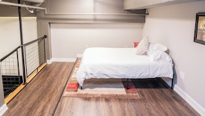 A bedroom with a bed, a red nightstand, a white wall, and a wooden floor.