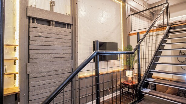 A staircase with metal railings and wooden steps, leading to a landing area with a desk and chair.