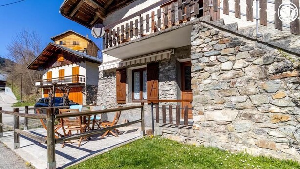 Un edificio de piedra con balcón, valla de madera y mobiliario exterior.