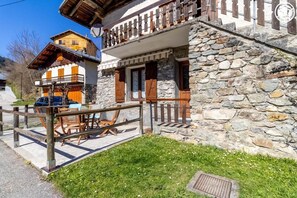 Un edificio in pietra con un balcone, una recinzione in legno e posti a sedere all'aperto.
