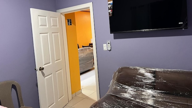 A room with a white door, a TV mounted on the wall, and a bed covered in plastic. - Casa de Vacaciones (La ceiba)