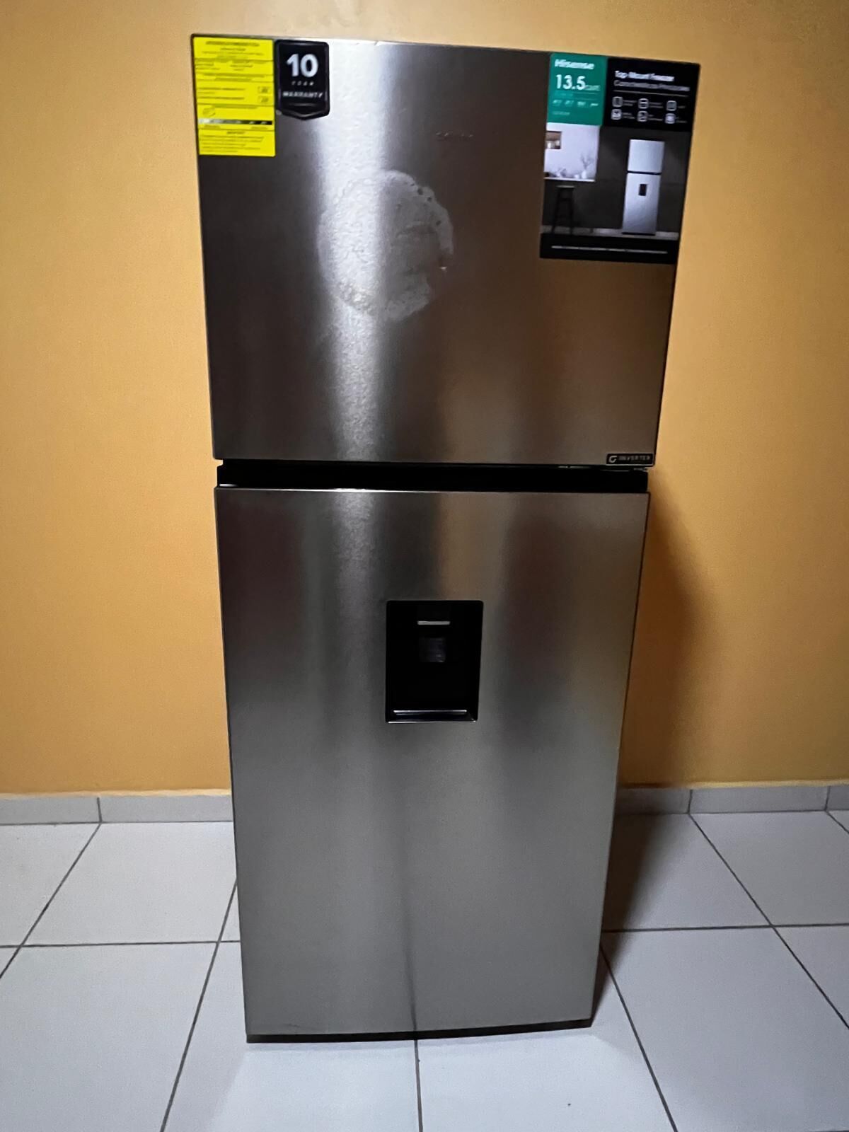 A stainless steel refrigerator with a 10-year warranty sticker, a digital display, and a control panel.