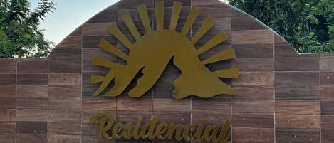 Ein Schild mit Sonne und Dinosauriersilhouette, mit dem Schriftzug 'Residencial El Dorado' auf Holz.