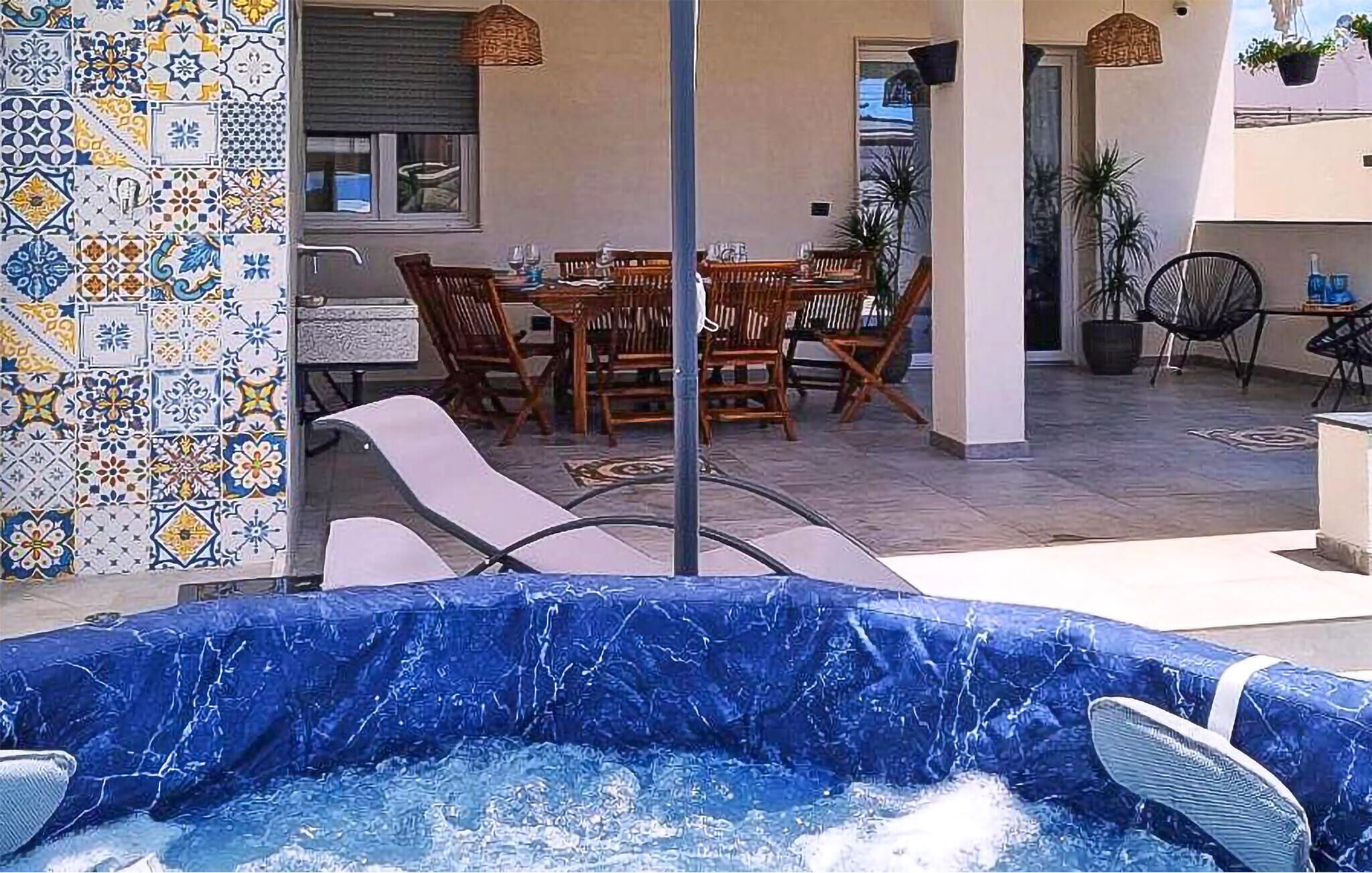 A pool area with a hot tub, outdoor seating, and a tiled wall with a geometric pattern.