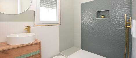 Ein Badezimmer mit rundem Spiegel, weißem Waschbecken, Toilette und Duschbereich mit strukturierter Wand.