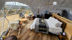 Ein gemütliches, helles Zimmer mit einem Bett, einem kleinen Tisch und einem Stuhl. Ein großes Fenster bietet Blick ins Freie.