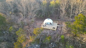 A geodesic dome structure with a wooden deck and seating area, surrounded by a forested landscape. - RIVER VIEW Cliff Dome Glamping @ White River, minutes to fishing, hikes! (Cotter)