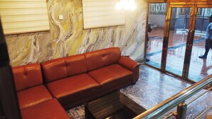 A lobby with a brown leather sofa, marble walls, a glass door, and a staircase with a metal railing. - SMILE-T CONTINENTAL HOTEL (Lagos)