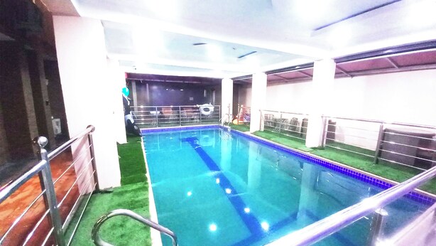 An indoor swimming pool with clear blue water, surrounded by a metal railing and a green artificial turf area. - SMILE-T CONTINENTAL HOTEL (Lagos)