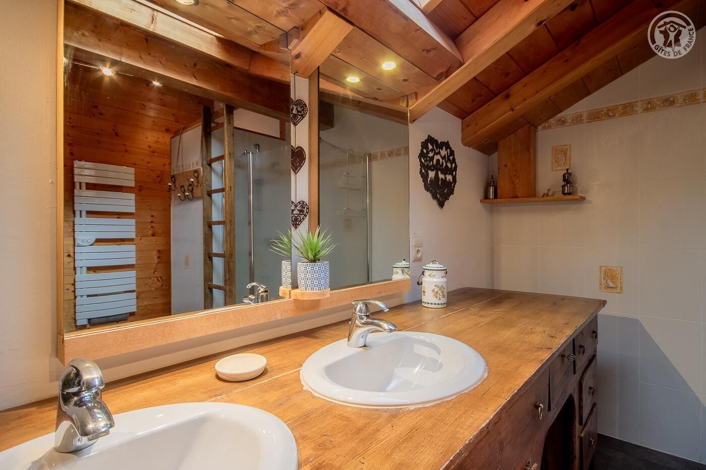 A bathroom with wooden beams, two sinks, a large mirror, and a small shelf with decorative items.