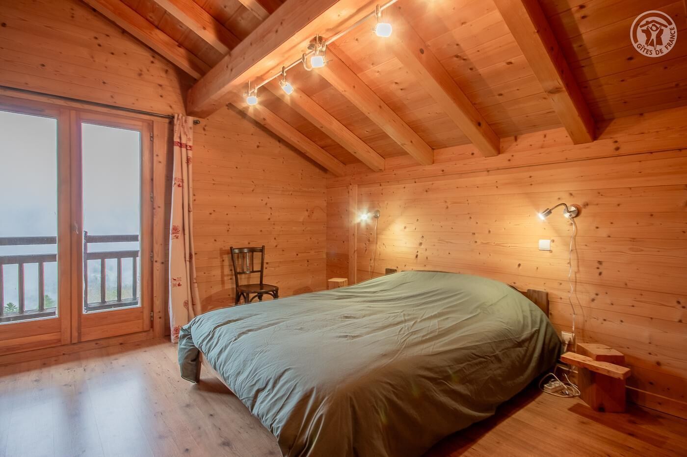 Une chambre dans un chalet en bois, comprenant un lit, une chaise, une table et un balcon.