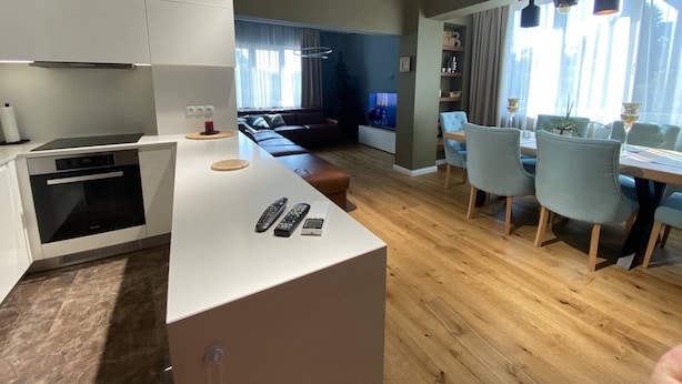 Une cuisine moderne dotée d’un îlot central, un coin repas avec une table et des chaises, et un salon avec un canapé et un téléviseur.