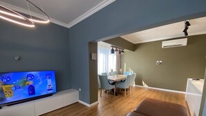 Un salon avec un téléviseur, un coin repas avec une table et des chaises, et un canapé en cuir marron.