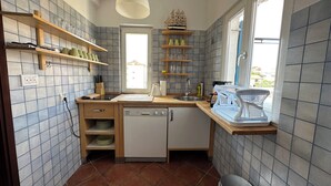 Une cuisine compacte dotée d’un plan de travail en bois, d’un lave-vaisselle intégré et d’étagères pour la vaisselle et les ustensiles.