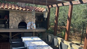Une terrasse extérieure dotée d’une cheminée en pierre, de meubles en osier et d’un sol carrelé.