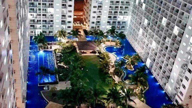 Un hôtel de grande hauteur, avec de nombreux étages, une piscine centrale et de nombreux espaces verts environnants.