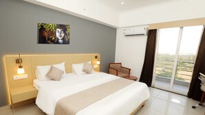 Habitación de hotel con una cama grande, lámparas de noche, una silla y vistas al exterior a través de un ventanal.