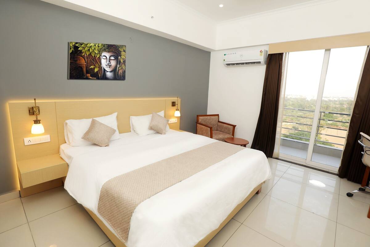 Habitación de hotel con una cama grande, lámparas de noche, una silla y vistas al exterior a través de un ventanal.
