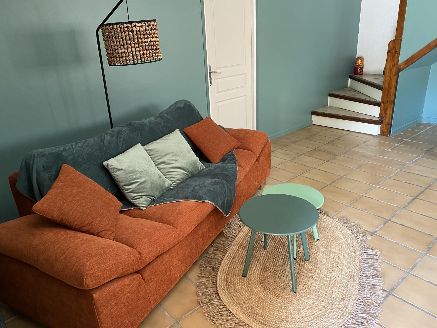 Ein Wohnzimmer mit braunem Sofa, zwei Kissen, einem kleinen grünen Tisch und einem gewebten Teppich.