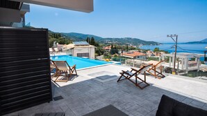 A rooftop terrace with a swimming pool, lounge chairs, and a view of the sea and hills. - The Bee Apartments Sea View (Lefkada)