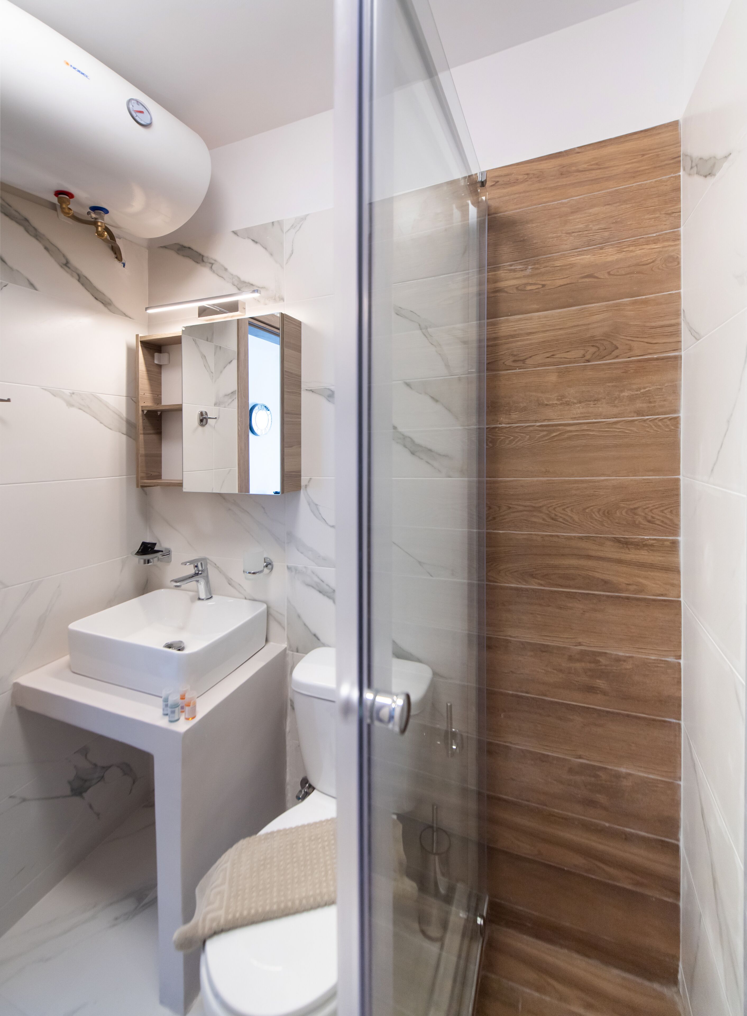 A modern bathroom with a glass shower enclosure, a white sink, and a marble-tiled wall.