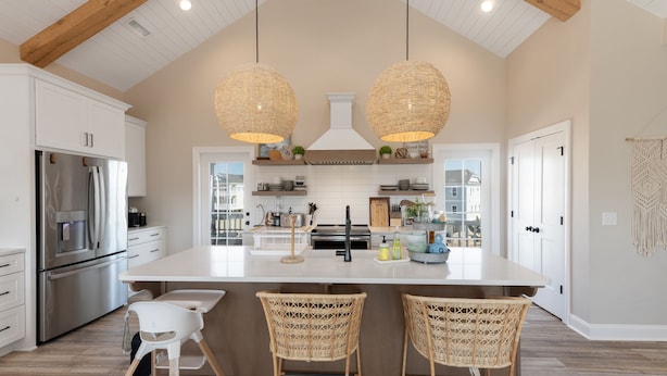 A spacious kitchen with a large island, two hanging wicker pendant lights, and a view of the backyard through the glass door.