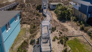 A beachside property with a wooden boardwalk leading to a white gazebo, surrounded by sandy terrain and sparse vegetation.