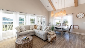 A spacious living room with a large L-shaped sectional sofa, a round coffee table, and a dining area with a wooden table and chairs.