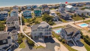 A coastal residential area with houses, a swimming pool, and a beach in the background.
