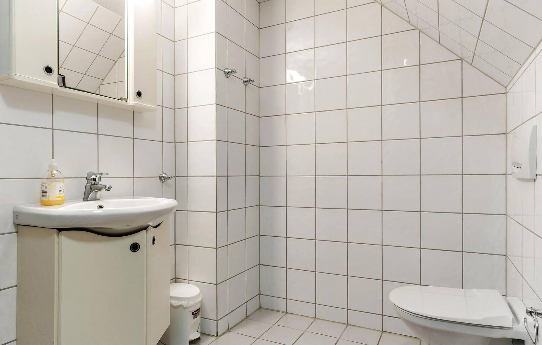 Une salle de bain comprenant un lavabo, des toilettes et un espace douche, le tout carrelé de blanc.