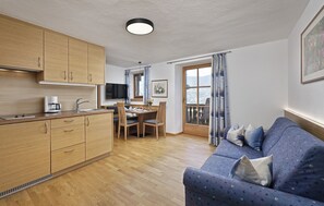 A modern kitchen with wooden cabinets, a dining area with a table and chairs, and a balcony with curtains. - Apartment 'Ifinger' with Mountain View, Shared Garden and Wi-Fi (Algund)