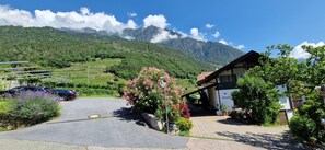 A rural hotel with a paved driveway, parked cars, and a mountain backdrop. - Apartment 'Ifinger' with Mountain View, Shared Garden and Wi-Fi (Algund)
