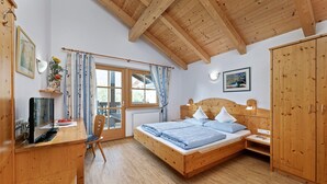 A bedroom with a wooden bed, a desk, a chair, a wardrobe, and a window with curtains.