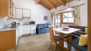 A kitchen with wooden cabinets, a dining table with chairs, a sofa, and a window with curtains.