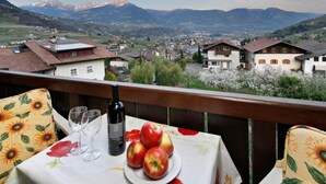 A balcony with a table set for two, a bottle of wine, and a plate of apples.
