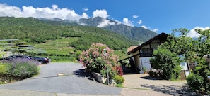 Un hôtel situé en zone rurale, avec une allée pavée, des voitures garées et une vue sur les montagnes en arrière-plan.