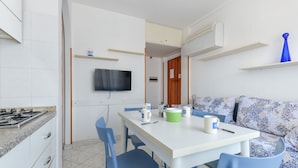 Una cocina moderna con comedor, un televisor montado en la pared y un sofá azul con cojines estampados.