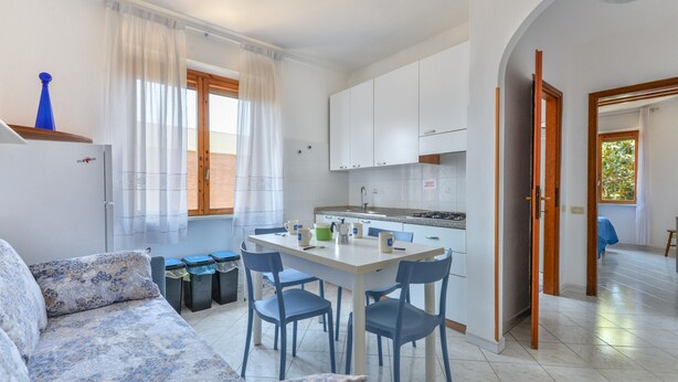 Una cocina moderna con armarios blancos, una mesa de comedor con sillas y un sofá con cojines estampados.