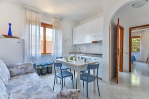 A modern kitchen with white cabinets, a dining table with chairs, and a sofa with patterned cushions.