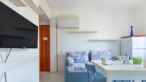Habitación compacta con sofá, mesa de comedor, sillas, televisor y una zona de kitchenette.