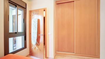 A bedroom with a bed, a window, a wooden wardrobe, and a door with a hanging rack.
