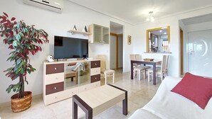 Una sala de estar moderna con un televisor de pantalla plana, un mueble de madera, una mesa de comedor con sillas, un espejo grande y una planta en maceta.