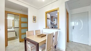Un comedor con una mesa y sillas, una cocina visible a través de una puerta abierta y una puerta blanca a la derecha.