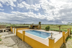 Una piscina con zona de patio, una estructura similar a una casa y vistas a un campo.