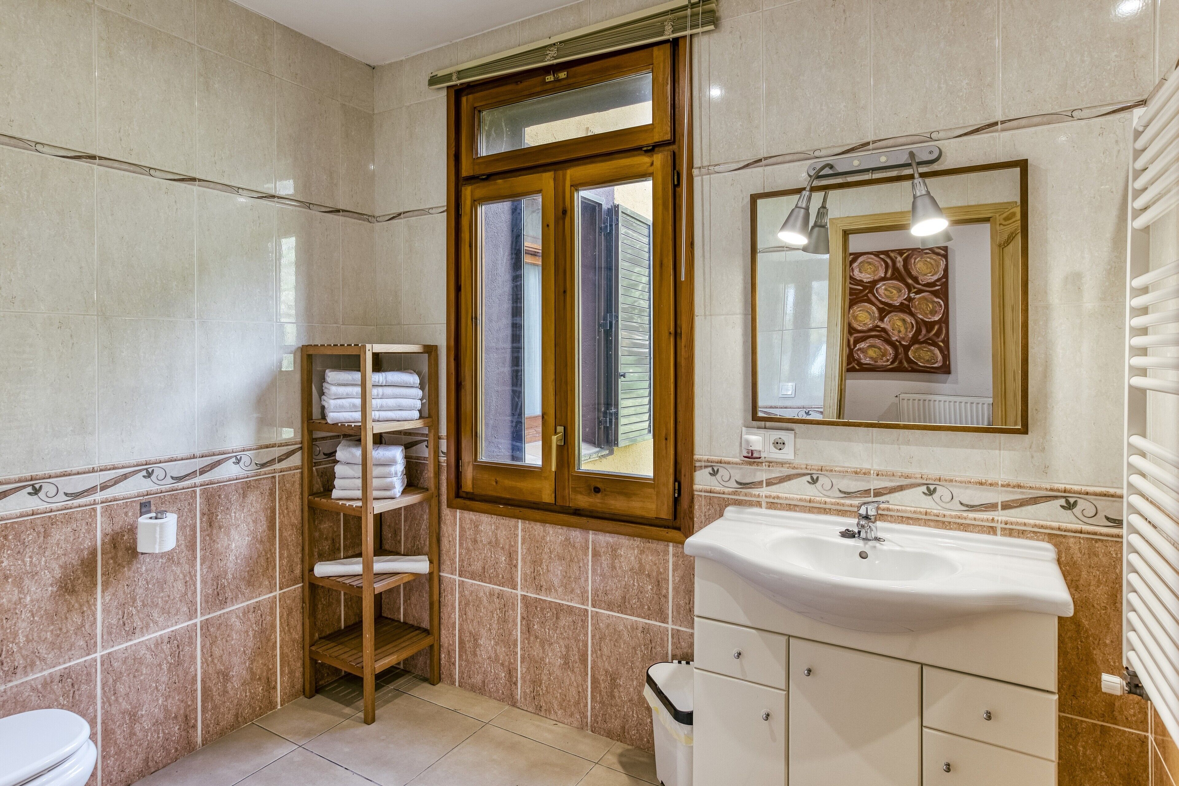A bathroom with a toilet, sink, towel rack, and a window with a view.