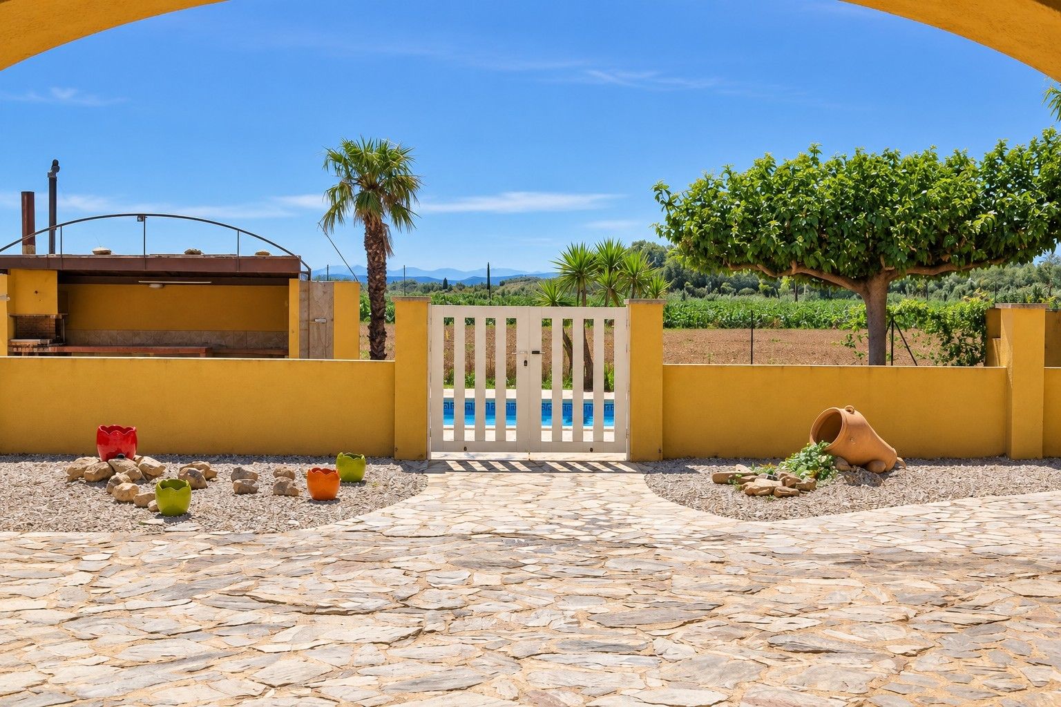 Ein von Pflastersteinen ausgelegter Innenhof mit Pool, Tor und Blick auf einen Weinberg.