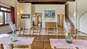Une salle à manger spacieuse avec des tables et des chaises en bois, un escalier menant à un niveau supérieur et un tableau accroché au mur.