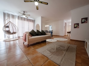 A modern living room with a sofa, hanging chair, two round tables, and a ceiling fan.