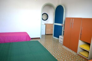 A room with two beds, a wardrobe, a small cabinet, and a door with a circular mirror.